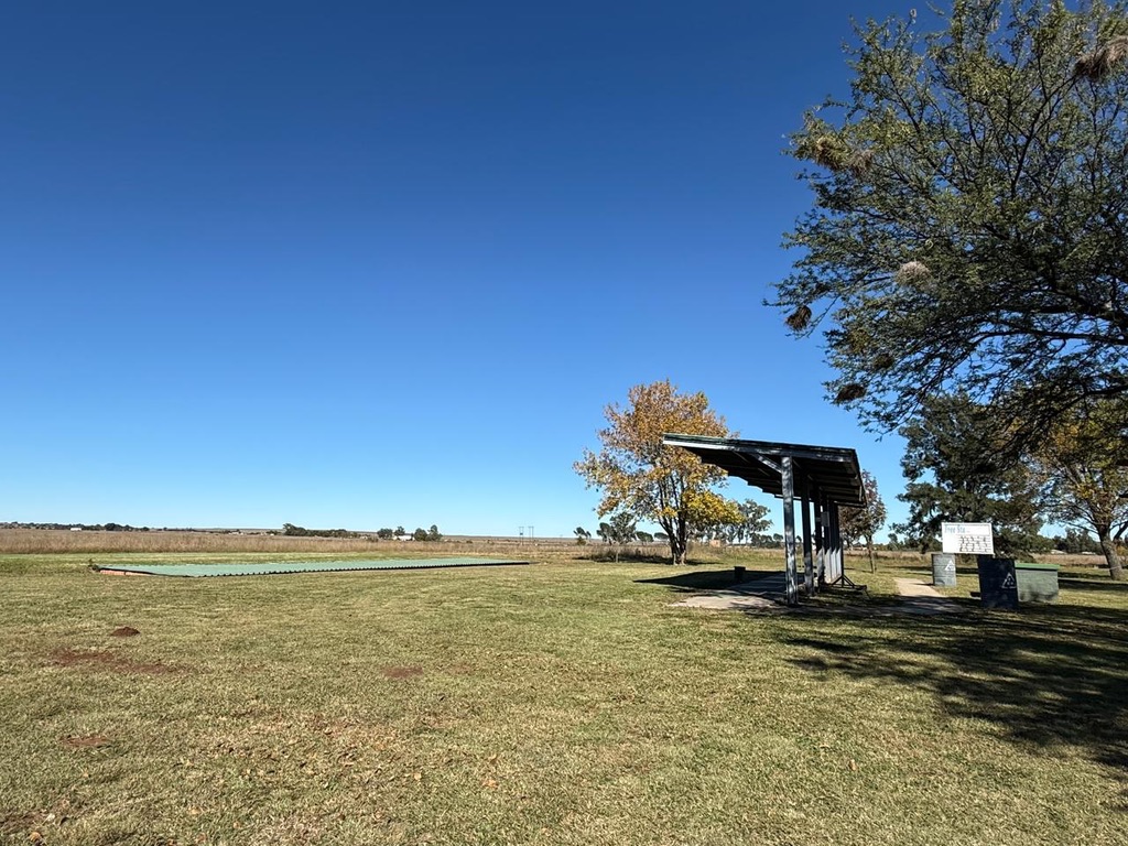 Open range with sheltered stand and autumn trees under a clear sky