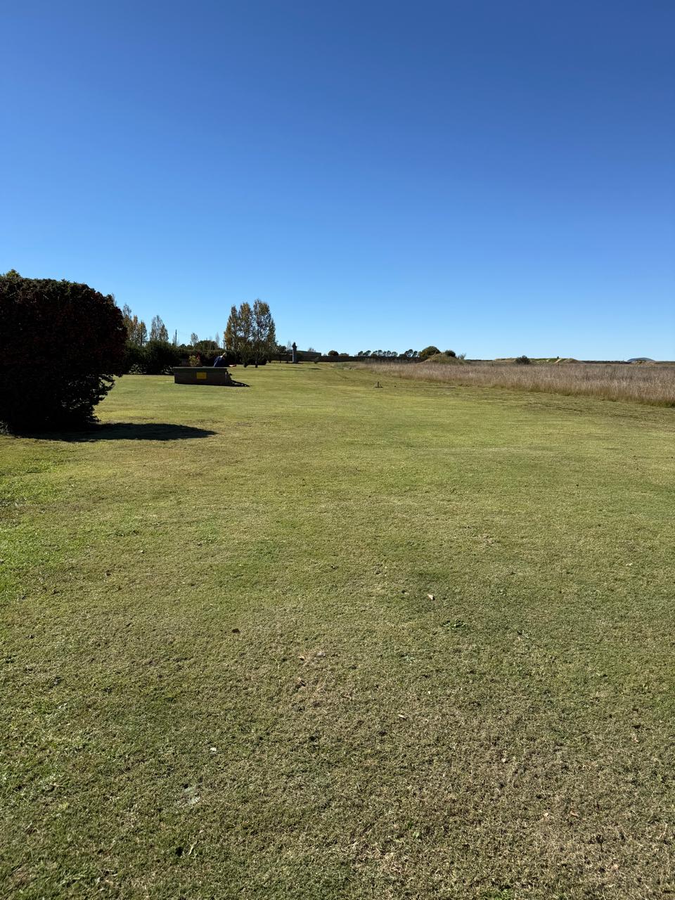 Wide green fairway leading downrange under a clear blue sky